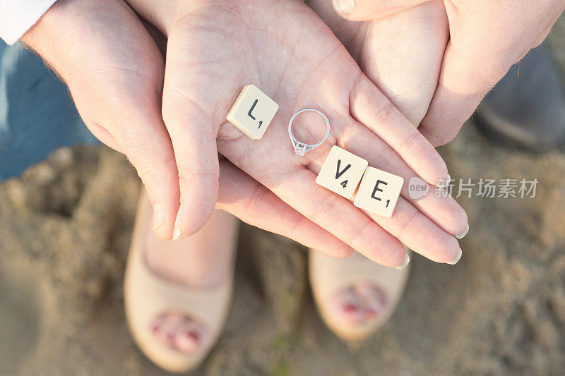 字母瓷砖和手上的订婚戒指