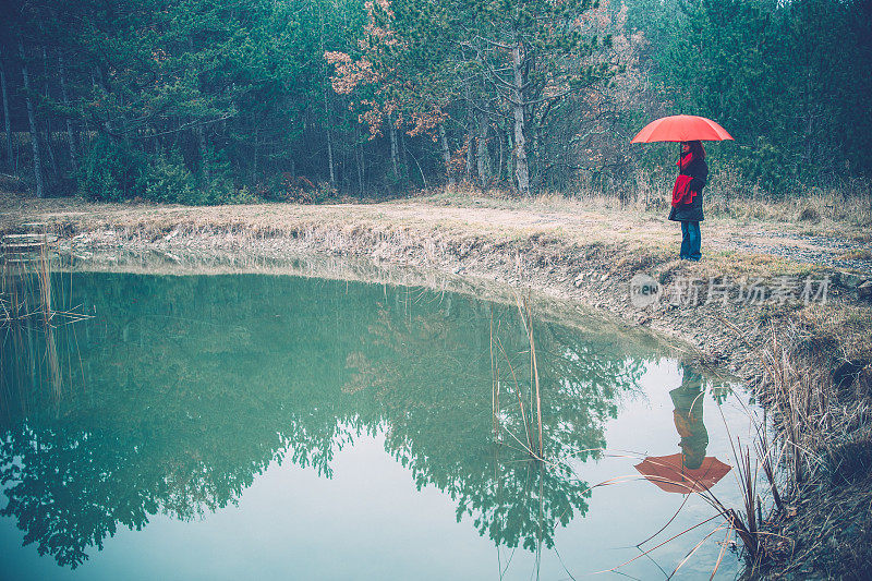 站在湖边，拿着雨伞的女人在大自然中