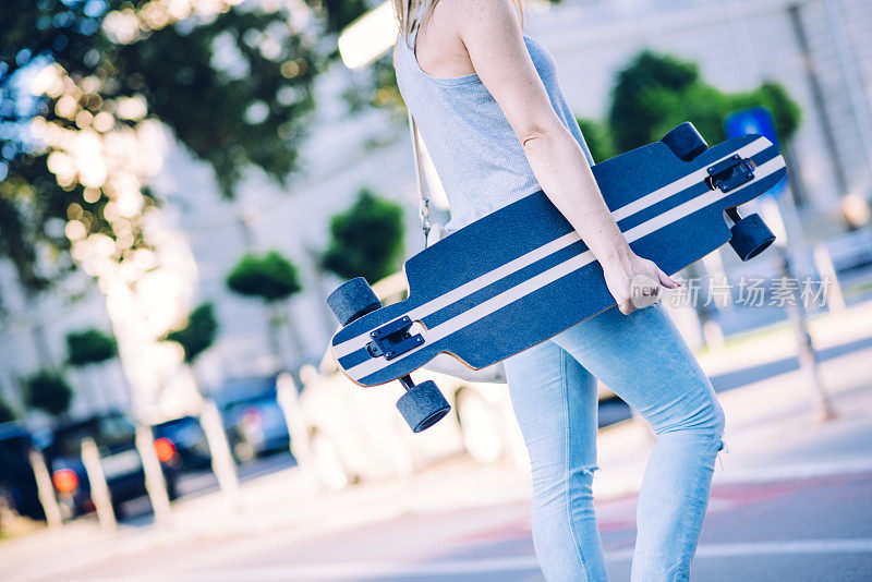 一个拿着滑板在城市里走的女人