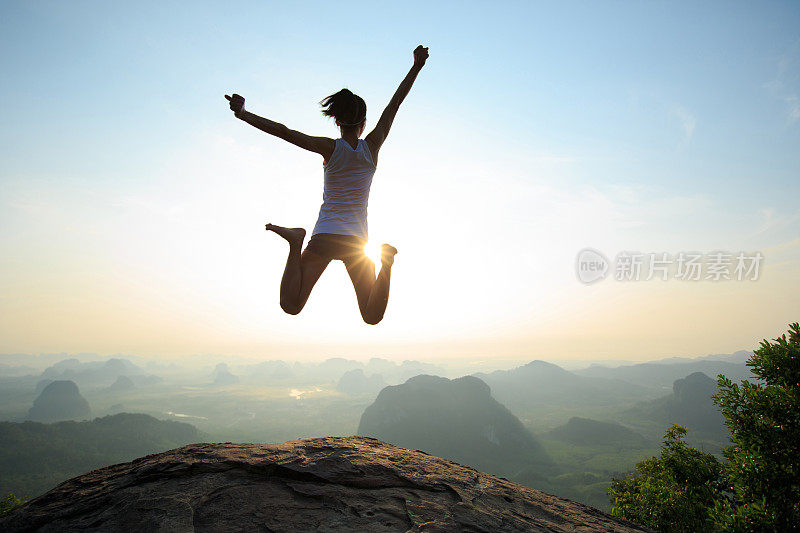 年轻女子跳跃在日出的落基山峰上，有自由、冒险、挑战、成功的观念
