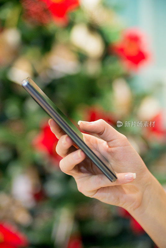 一个女人用智能手机和圣诞树发短信的特写