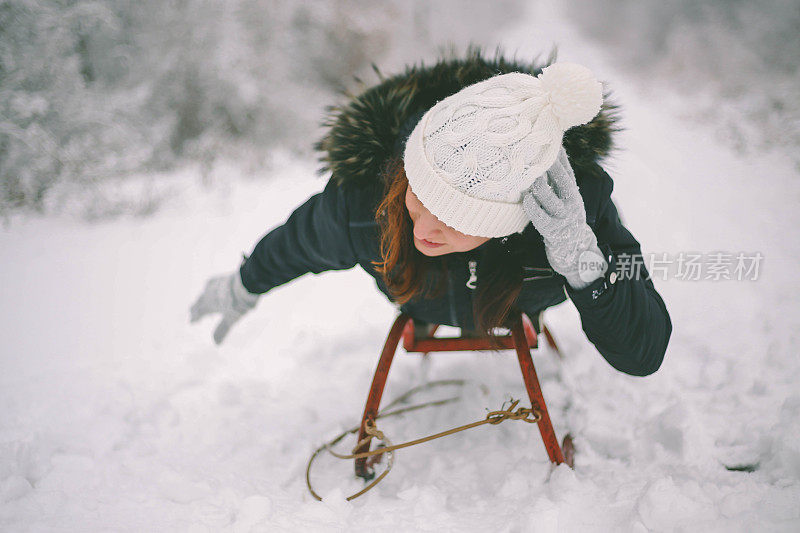 快乐的年轻女子在一个快速的雪橇骑下冰冷的斜坡