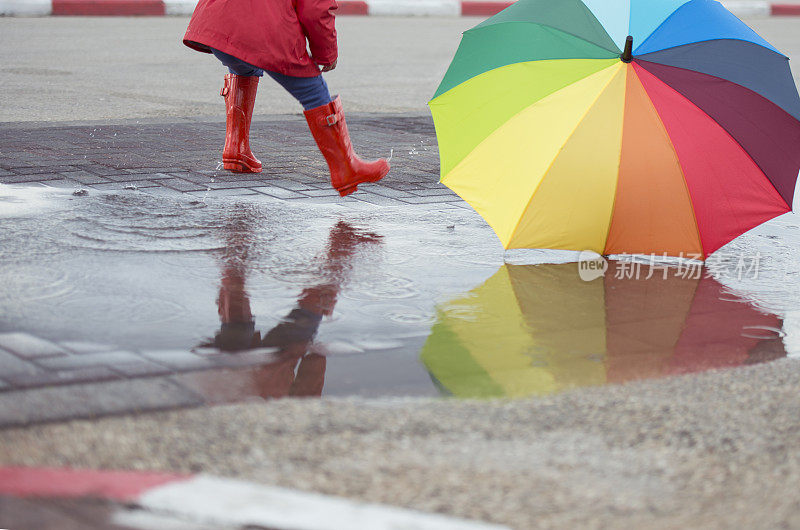 带着彩色伞在泥泞的水坑里跳跃的孩子。