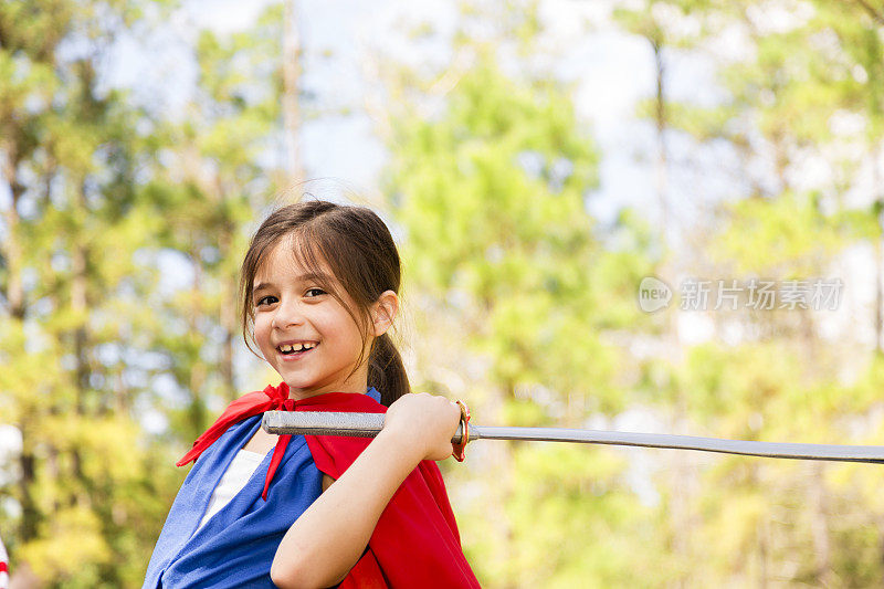 可爱的小女孩在玩“假装”。英雄,斗篷,剑。