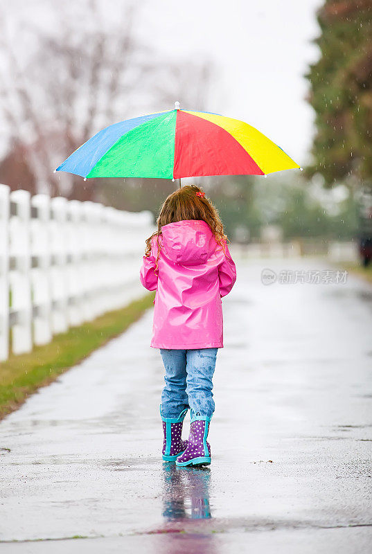 带着彩虹伞走在雨中的少女