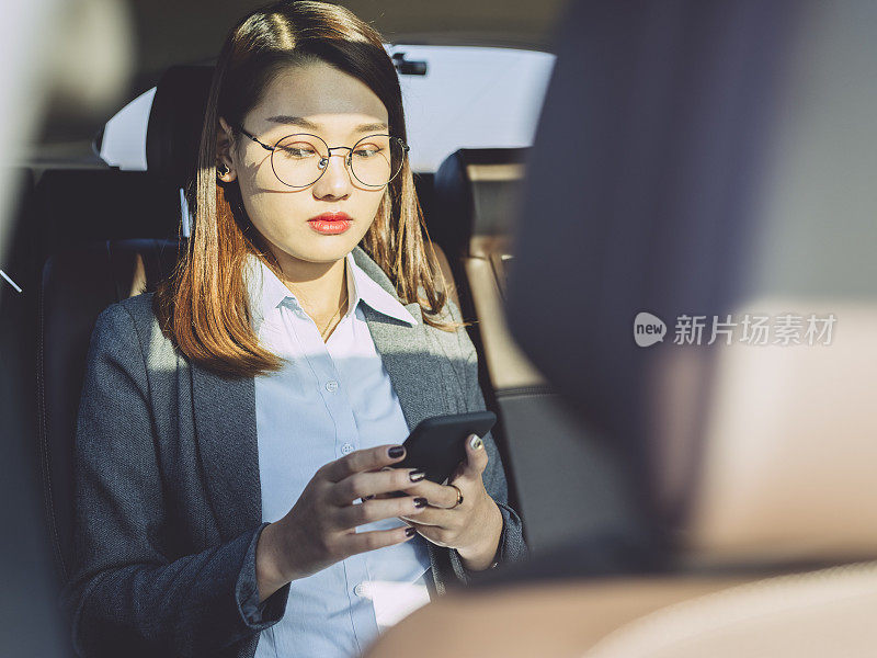年轻女商人在汽车后座上用手机