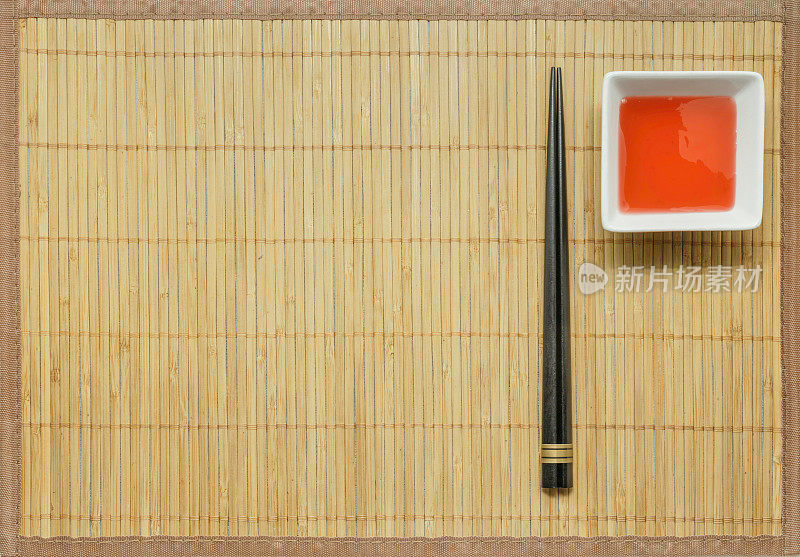 黑色木筷子和甜酸酱竹席背景。