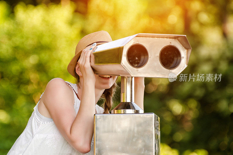 戴帽子的女孩看着大望远镜。背景是绿色的。前视图