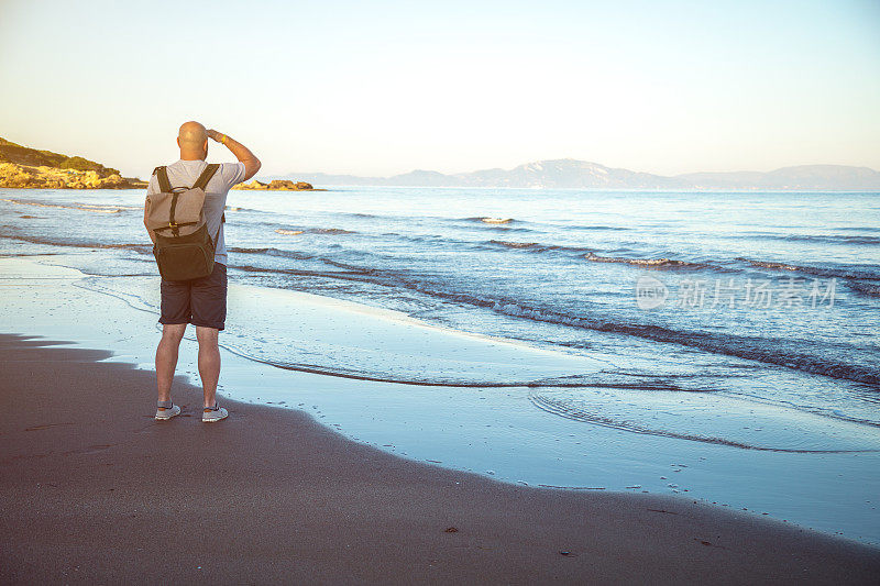 背着背包的男性旅行者在海边观看日出