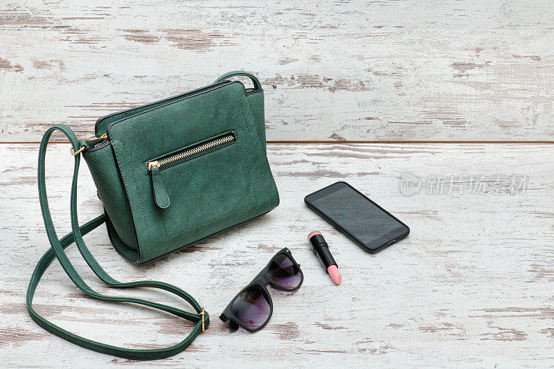 绿色小女士手提包，太阳镜，口红和智能手机。时尚的概念
