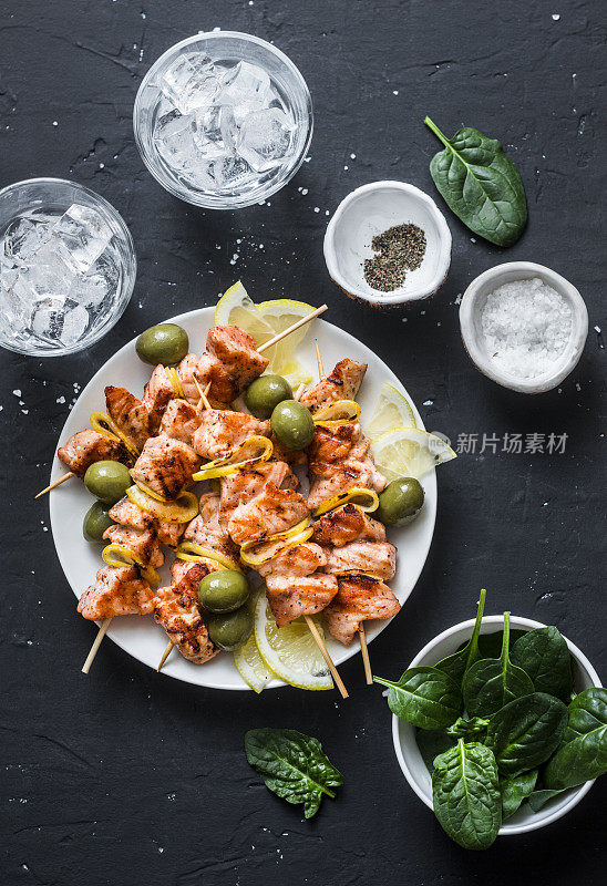 三文鱼串，橄榄，菠菜，冰水-小吃桌。烤鲑鱼串在一个黑暗的背景，俯视图