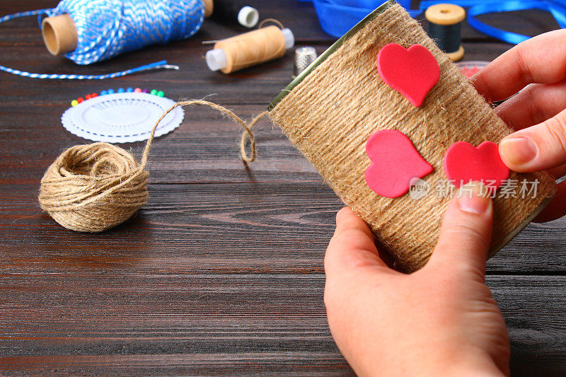 双手将心形贴在木桌上用绳子包着的铁罐上。手工制作的。