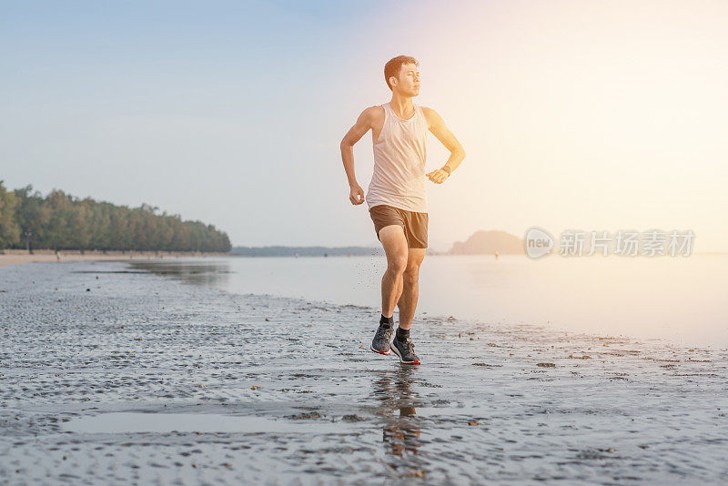 年轻的亚洲男子在海滩上奔跑，夕阳为背景