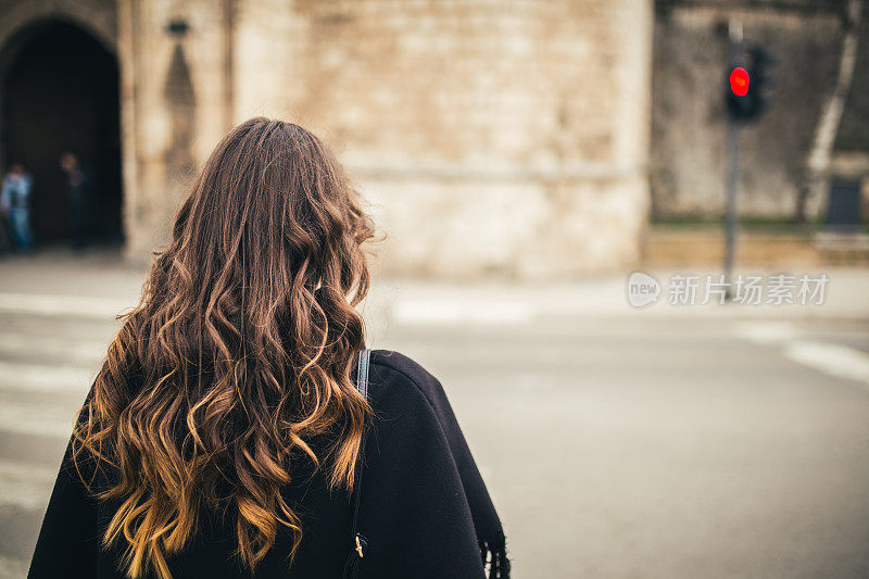 美丽的长发女孩走过城市，站在人行横道前。
