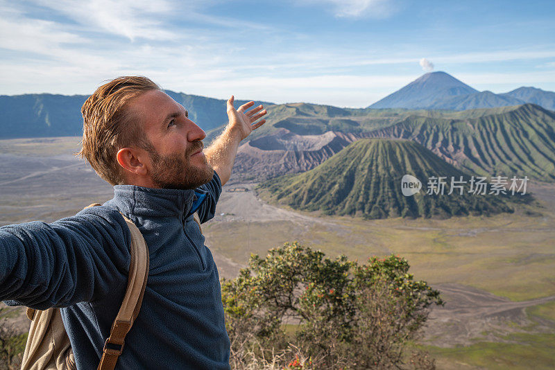 在印度尼西亚，年轻人徒步旅行，手臂伸开站在火山的山顶上，人们旅行的乐趣，冒险的概念，成功和成就