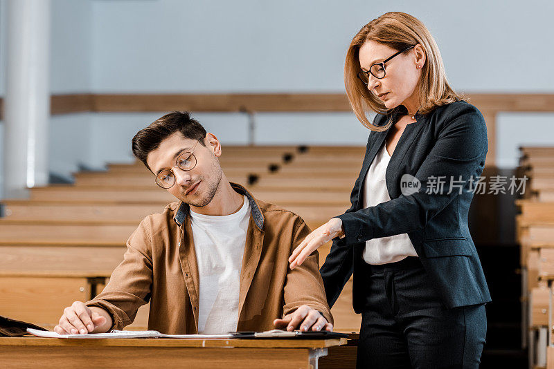 女大学老师在教室里看着戴眼镜的男学生写作考试
