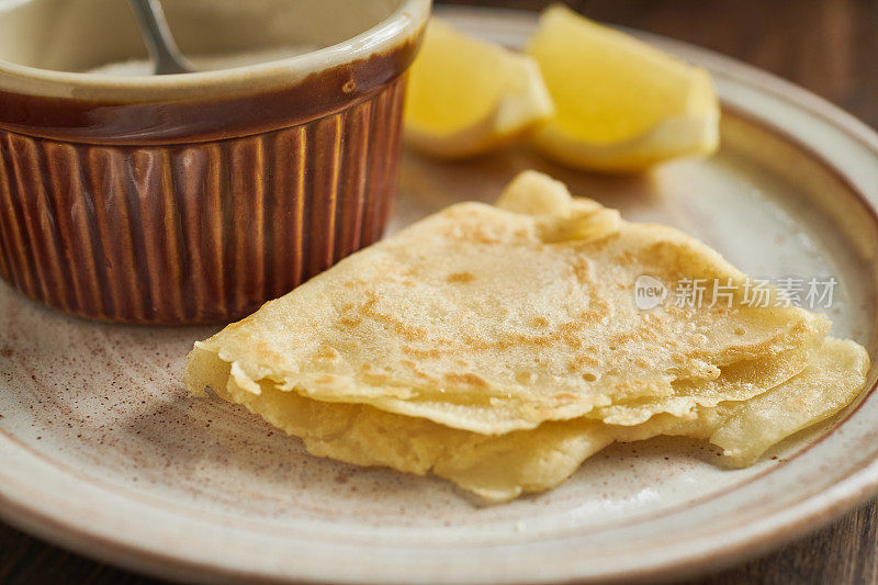 盛有薄煎饼、柠檬角和一碗糖的盘子。