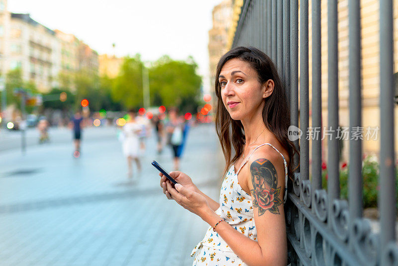 美丽的纹身女人在城里用智能手机