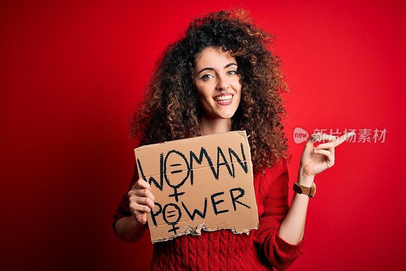 一头卷发、穿洞的激进分子举着印有女性权力信息的海报，非常高兴地用手和手指向一边