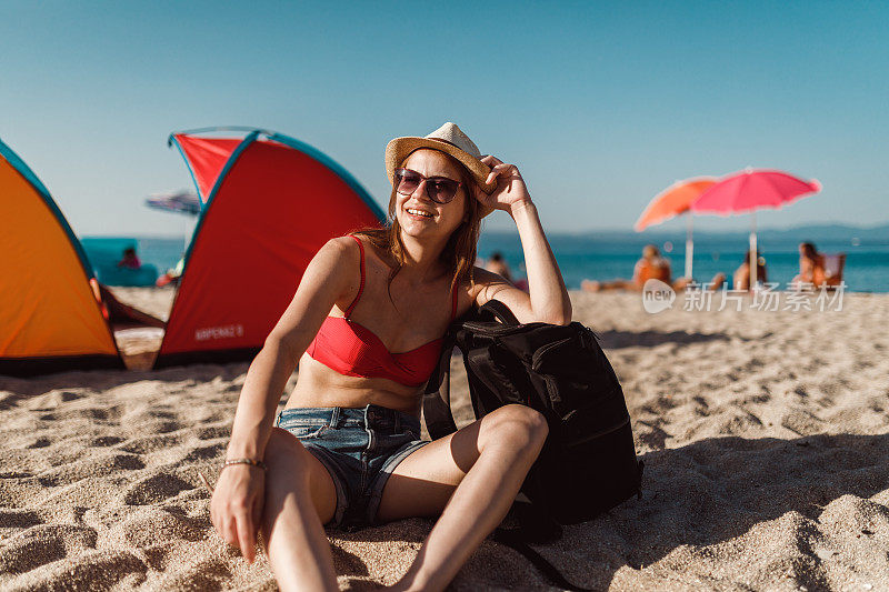 在一个阳光明媚的日子里，一个女人坐在海滩的帐篷旁边
