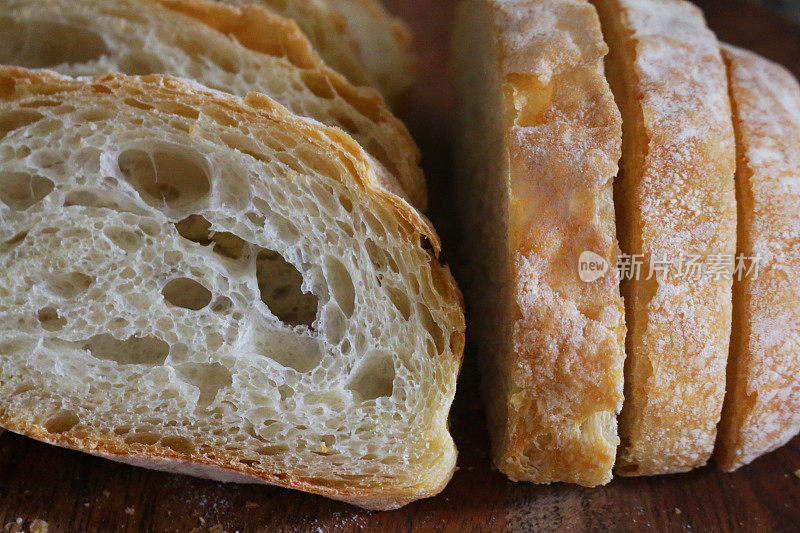 特写:切成薄片的自制夏巴塔面包，放在木砧板上，金黄色，刚出炉的面包，切成薄片的硬面包