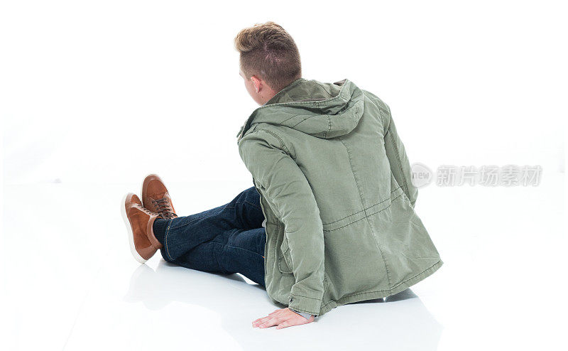 白人年轻男性坐在地板上的白色背景，穿着暖和的衣服