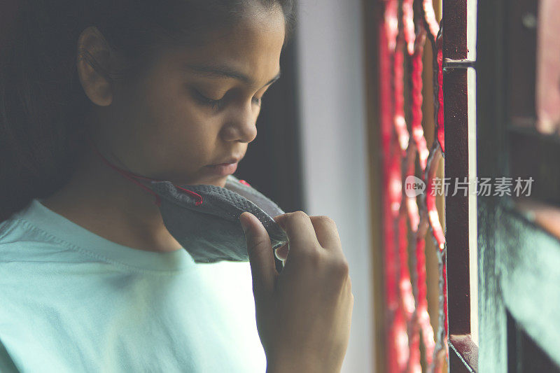 这个悲伤的女孩正在保护自己，戴着口罩，在家里自我隔离。