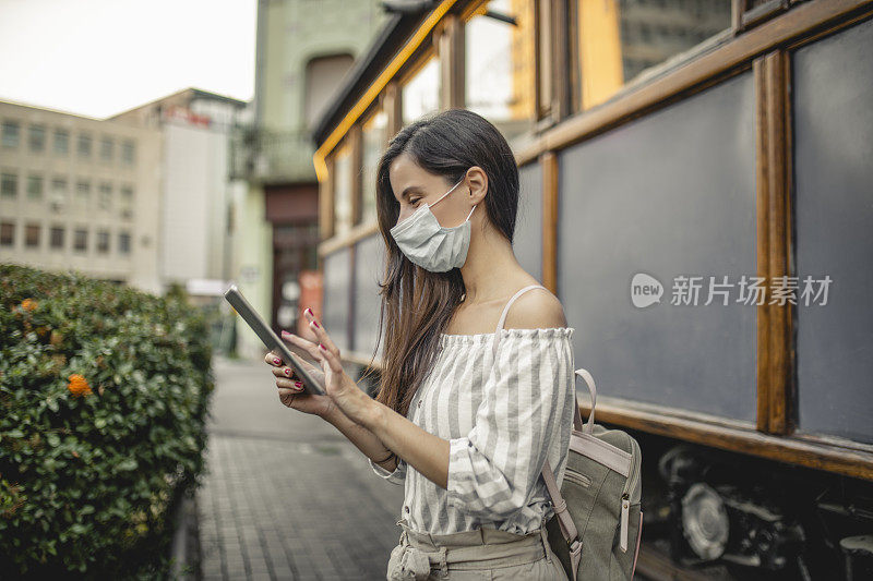 时尚女性的肖像与医用口罩使用数字平板电脑在疫情期间的户外