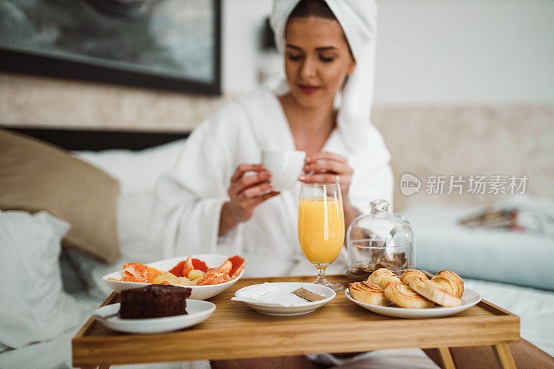 一个女人用托盘吃早餐，在床上喝咖啡