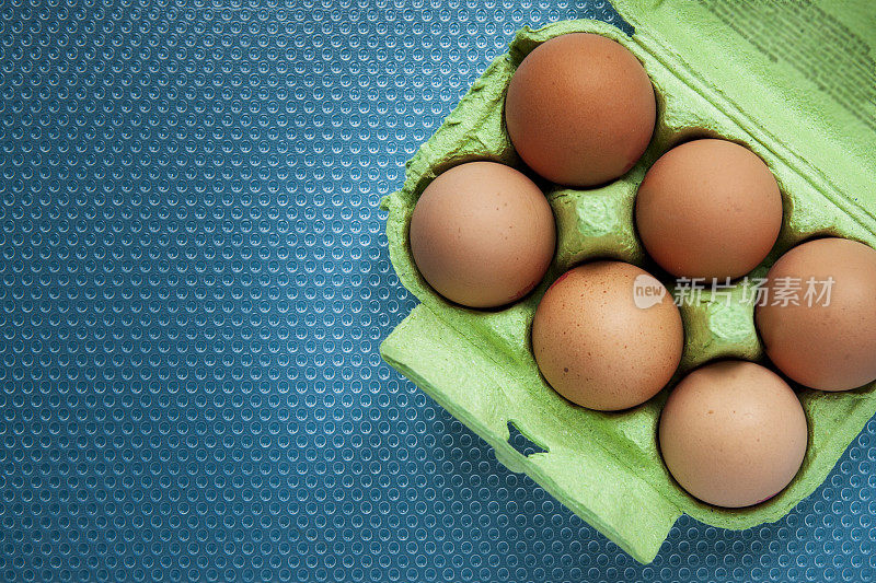 6个鸡蛋放在一个绿色的硬纸板鸡蛋盒上，上面有一个蓝色的塑料凹纹纹理表面