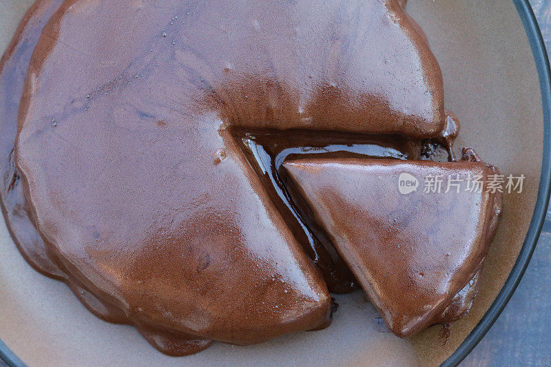 热的，切片的巧克力软糖蛋糕覆盖了一层厚厚的巧克力软糖酱，在一个蓝色的木纹背景下的盘子，俯瞰