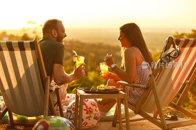 年轻的夫妇在甲板上享受夏日，鸡尾酒和充气