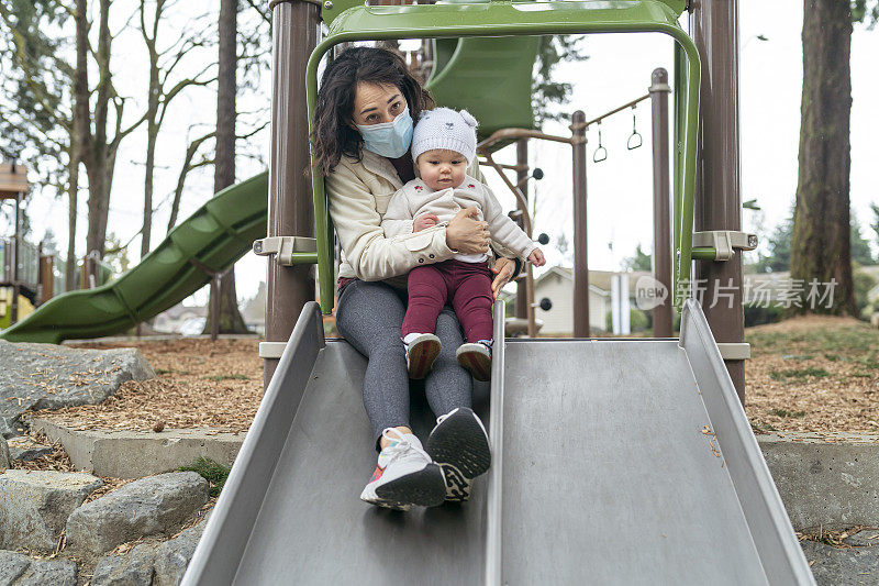 混血妈妈戴着防护面具和蹒跚学步的女儿在公园玩耍
