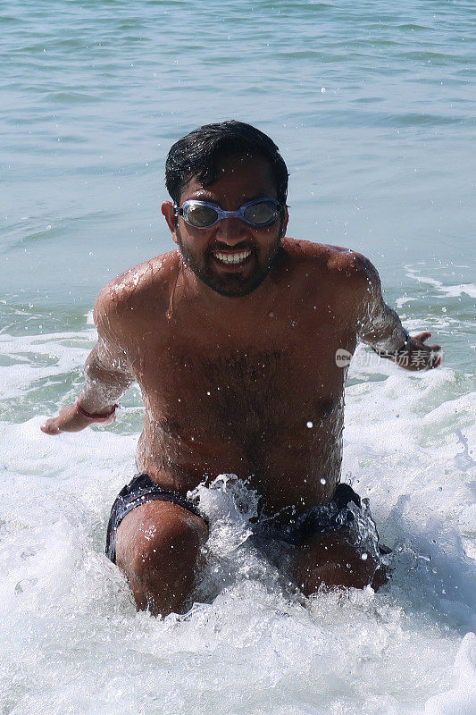 印度果阿巴洛勒姆海滩，一名印度男子在海滩度假，坐在印度洋上，戴着护目镜，笑得很开心