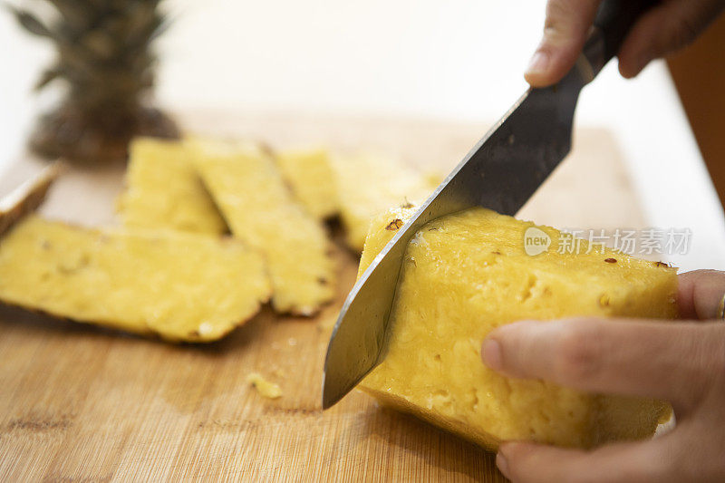 一个女人的手用刀在一块板上切菠萝片的特写