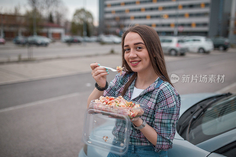 一个微笑的年轻女子正在吃塑料盒里的沙拉