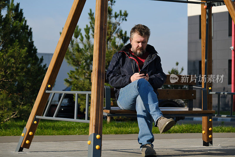 一个成熟的男人坐在长凳上用手机