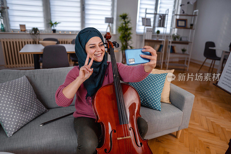 年轻的穆斯林妇女在家里拉大提琴时自拍