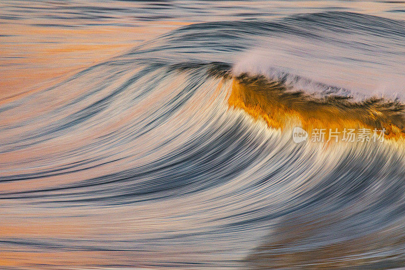 在海滩日落时，光滑的金色海浪反射出明亮的天空