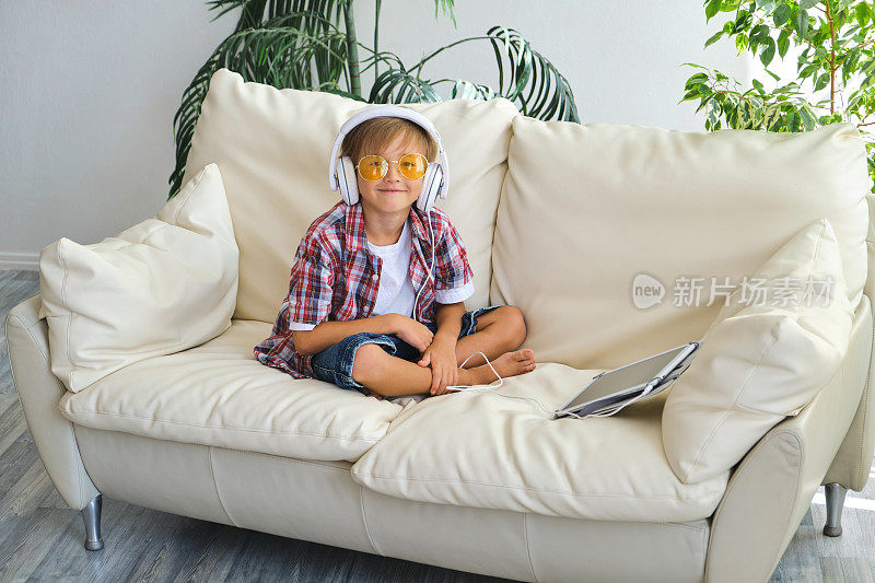 可爱的小男孩带着耳机和平板电脑在家听有声读物