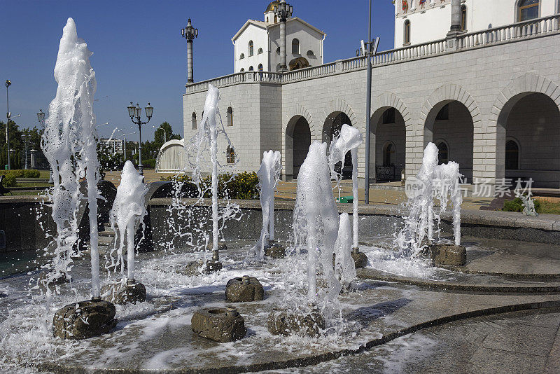 喷泉中飞溅的水花映衬着一座白色教堂。只有喷泉水的自然纹理。炎热夏季巨浪的影响。阳光明媚的日子里水花四溅的特写。