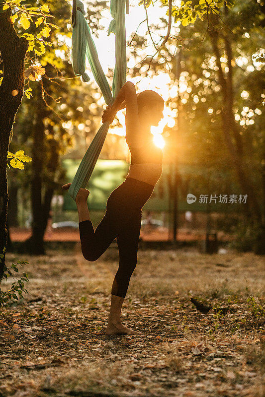 女人在日落时用空中丝绸做瑜伽