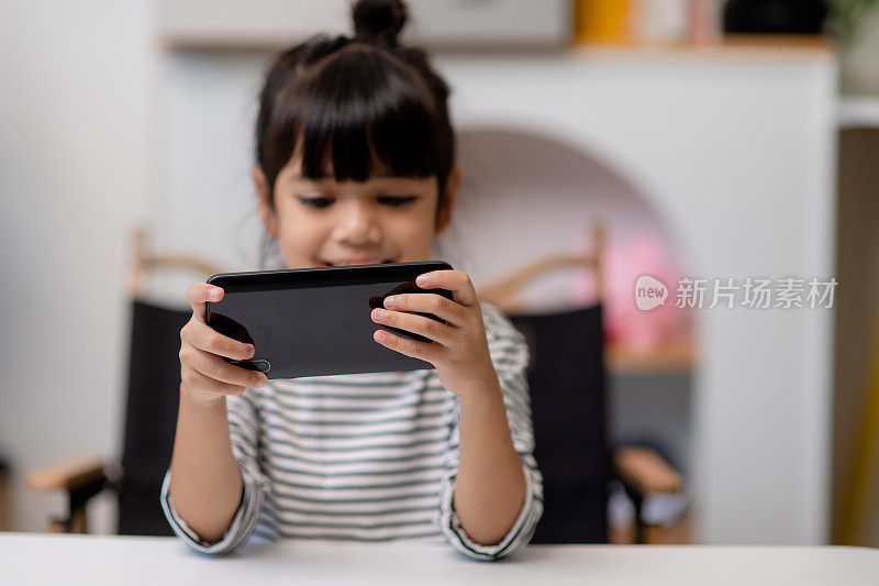 可爱的小女孩坐在客厅的沙发上使用智能手机。孩子在家里用手机上网、上网、看动画片