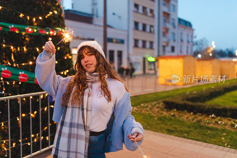 美丽的年轻女子拿着烟花在户外的一棵大圣诞树前