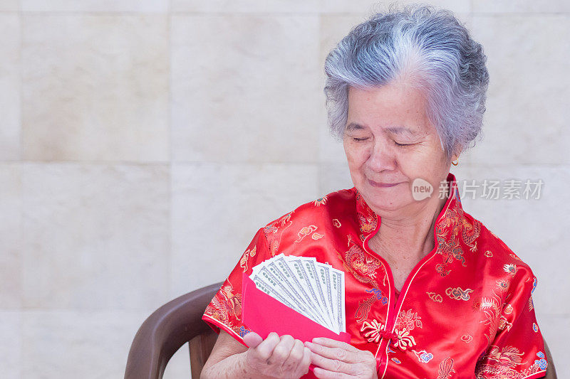 一名身穿红色旗袍的亚洲老妇人手里拿着一个装有美元的红包。