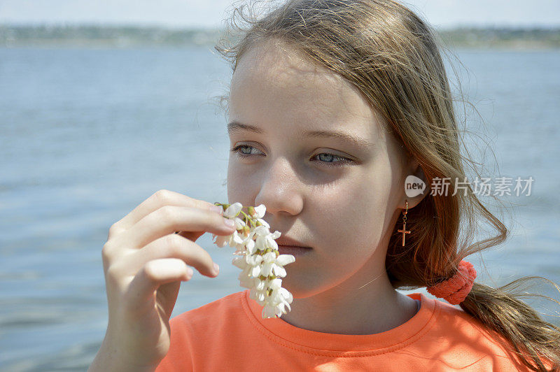 美丽的女孩拿着一朵白色的金合欢花，背景是蓝色的大海