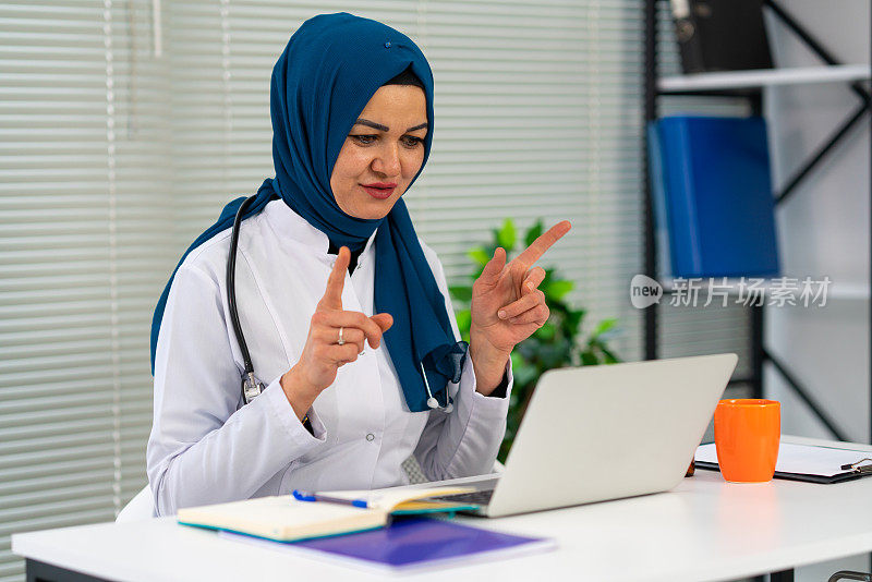 医生在线咨询病人，戴着头巾的穆斯林妇女远程用笔记本电脑进行视频通话，坐在现代化的诊所办公室里咨询病人