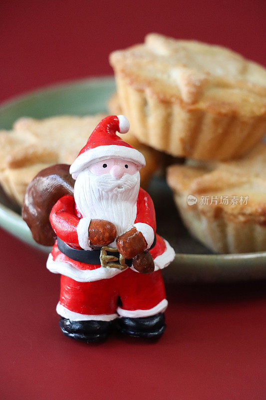 特写微型图像，圣诞老人雕像站在绿色盘子上的三个肉馅饼旁边，红色背景，重点放在前景，圣诞食品概念