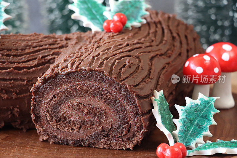 全画幅图像，以软糖蘑菇、冬青叶和红浆果装饰的巧克力圣诞原木蛋糕放在木板上，瑞士卷海绵，巧克力甘纳奇填充，天然树皮图案蚀刻成巧克力奶油糖霜，圣诞森林场景