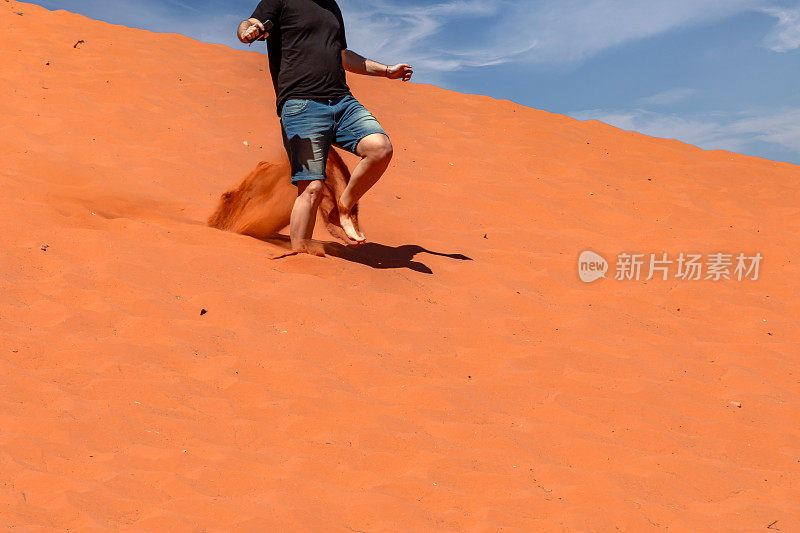 一个游客正从沙丘上跑下来，踢起尘土